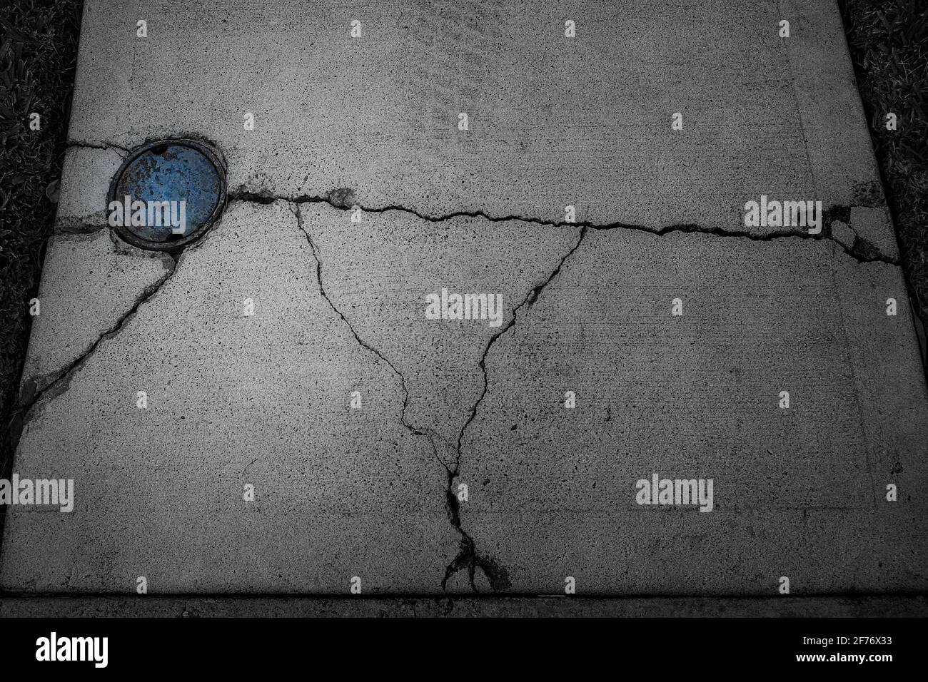 Abstrait, principalement photo en noir et blanc d'un trottoir en béton fissuré et brisé avec une couverture principale d'eau bleue. Banque D'Images