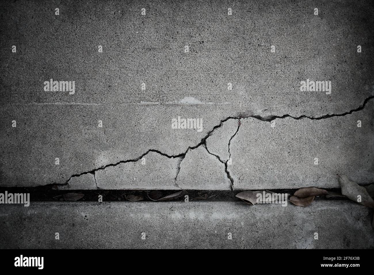 Photographie abstraite en noir et blanc d'un trottoir en béton fissuré et brisé où les fissures sont mises en évidence et sont le principal intérêt. Banque D'Images