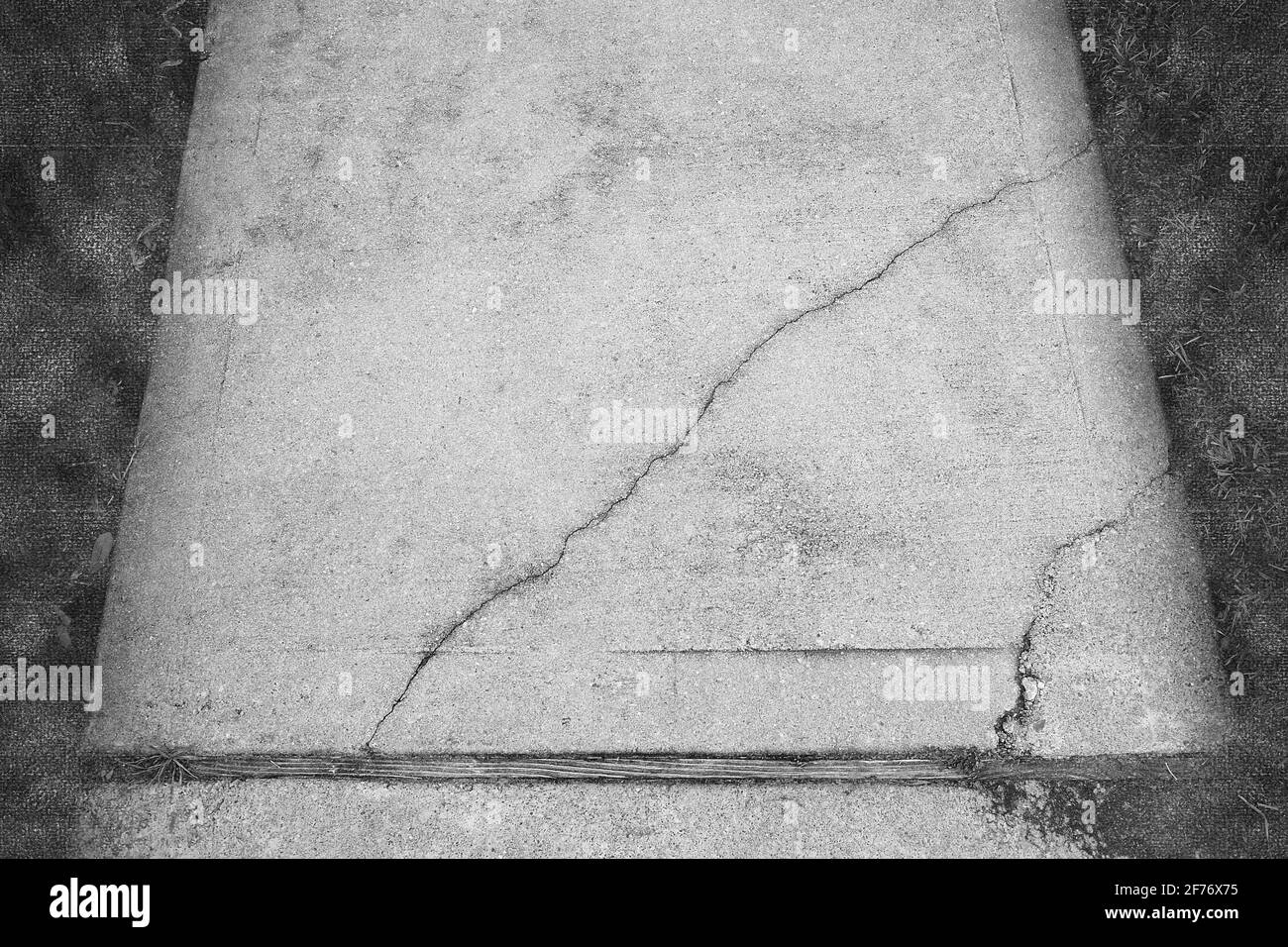 Photographie abstraite en noir et blanc d'un trottoir en béton fissuré et brisé où les fissures sont mises en évidence et sont le principal intérêt. Banque D'Images