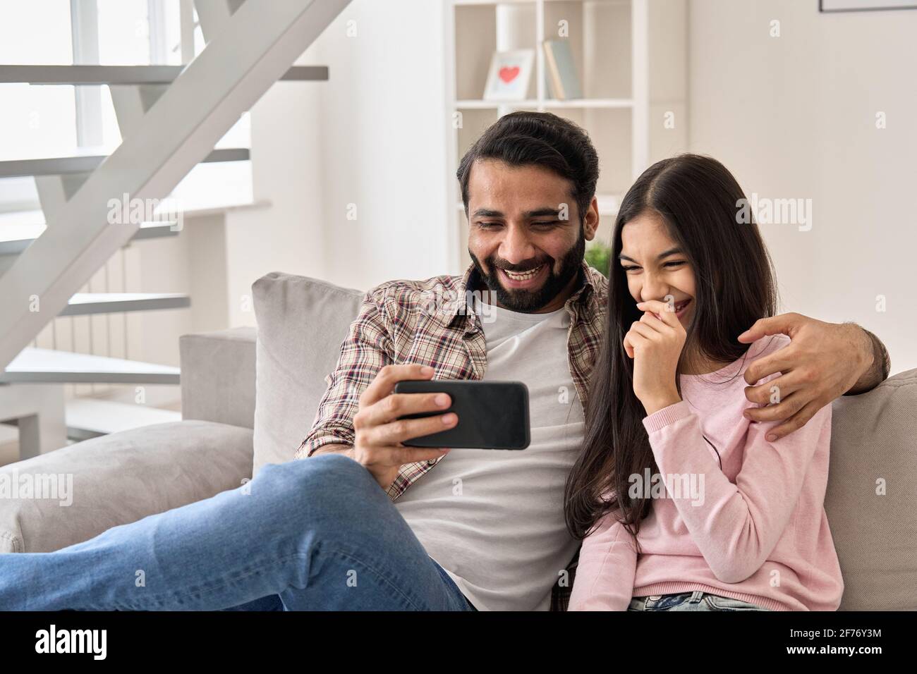 Père indien heureux avec une fille adolescente s'amusant à utiliser le téléphone à la maison. Banque D'Images