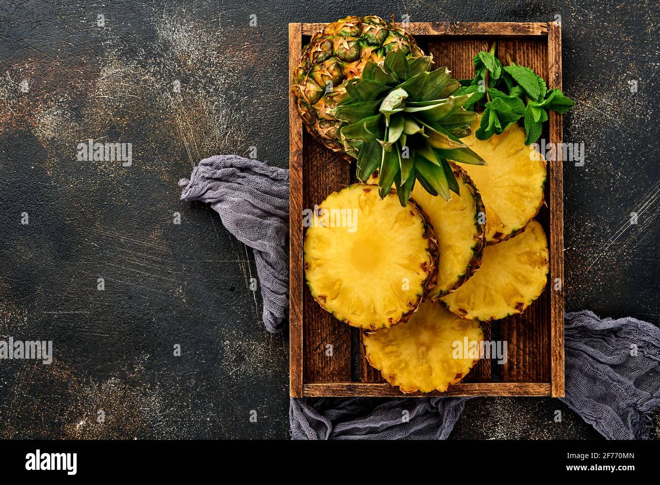 Émincé d'ananas mûr dans une boîte en bois sur fond de pierre brun foncé. Fruits tropicaux. Vue de dessus. Espace libre pour le texte. Maquette. Banque D'Images