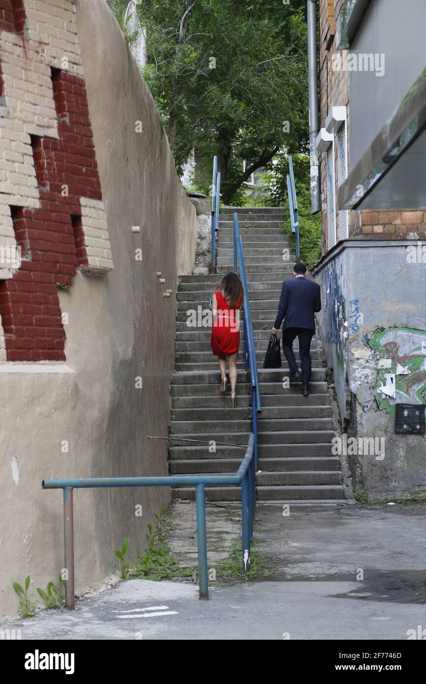 Femme en robe rouge et homme en costume monter les escaliers les uns à côté des autres, en parallèle, séparés par une rambarde. Concept de cheminement de carrière de l'inégalité des sexes Banque D'Images