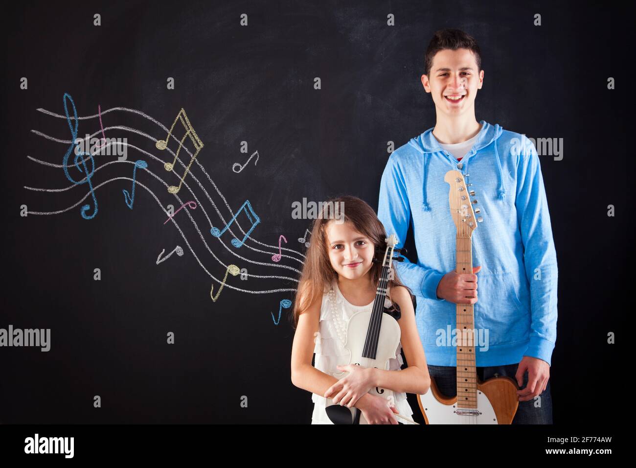 Frère et sœur jouant un instrument de musique à côté d'un tableau noir Banque D'Images