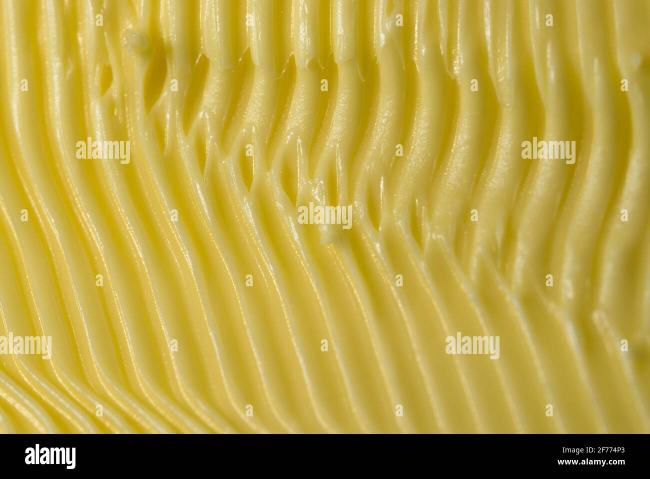 Fond de margarine sur le thème de la nourriture. Façonnés dans des rainures jaunes détaillées par un couteau de cuisine dentelé utilisé pour l'étaler sur le pain. Texture plein format. Banque D'Images