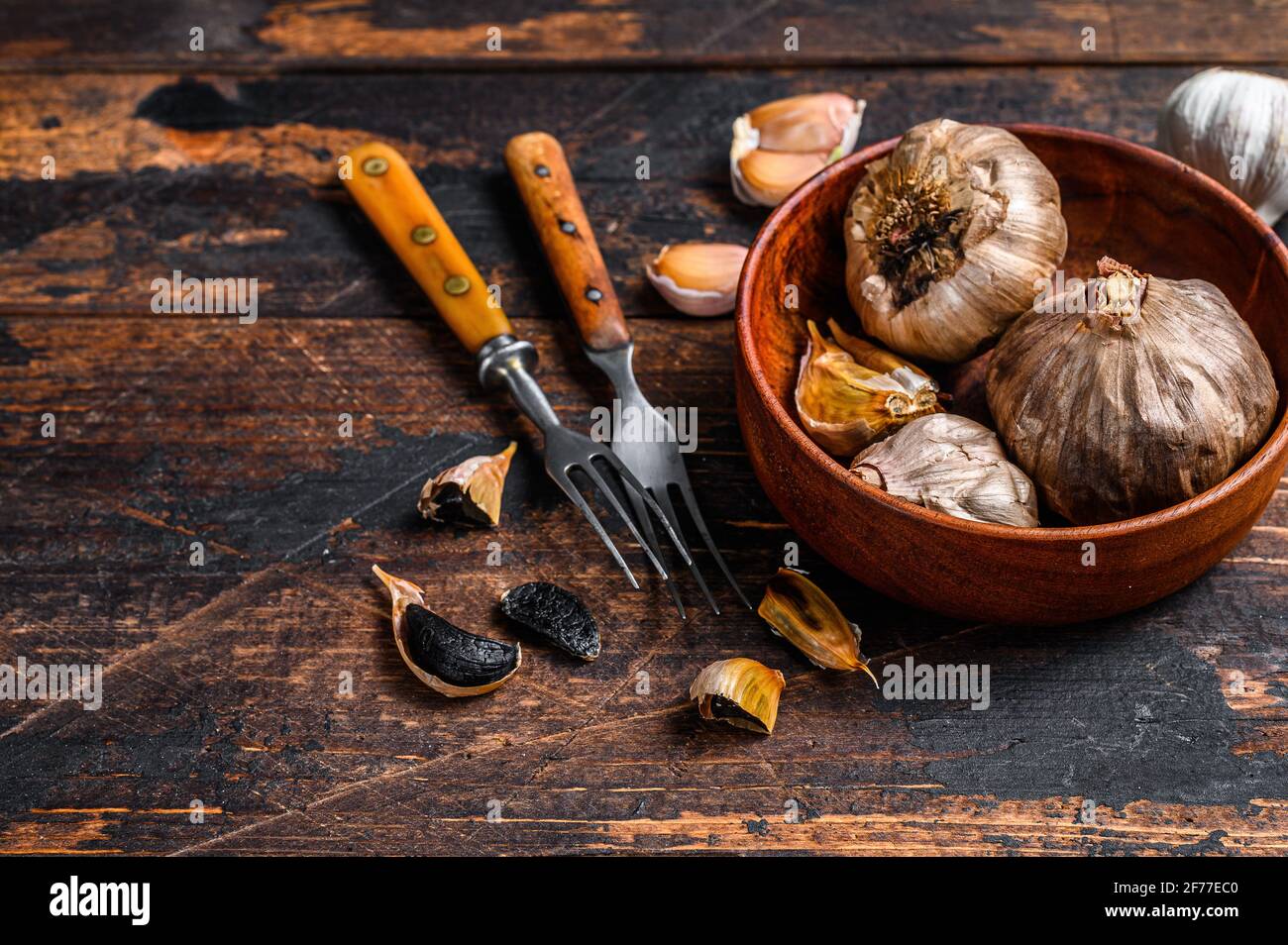 Bulbs and cloves of fermented black garlic in a plate. Dark wooden background. Top view. Copy space Banque D'Images