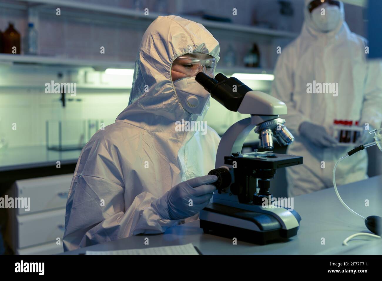 Scientifique en vêtements de travail de protection examinant les échantillons à travers le microscope à le tableau dans le laboratoire chimique Banque D'Images