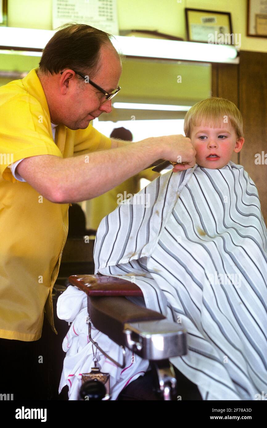 Homme Des Annees 1970 Coiffeur Coupant Les Cheveux Sur Un Jeune Garcon Blond Assis Dans La Chaise De Coiffure Avec Une Expression Faciale Incertaine Kj71 Lga001 Hars Old Fashion 1 Jeune