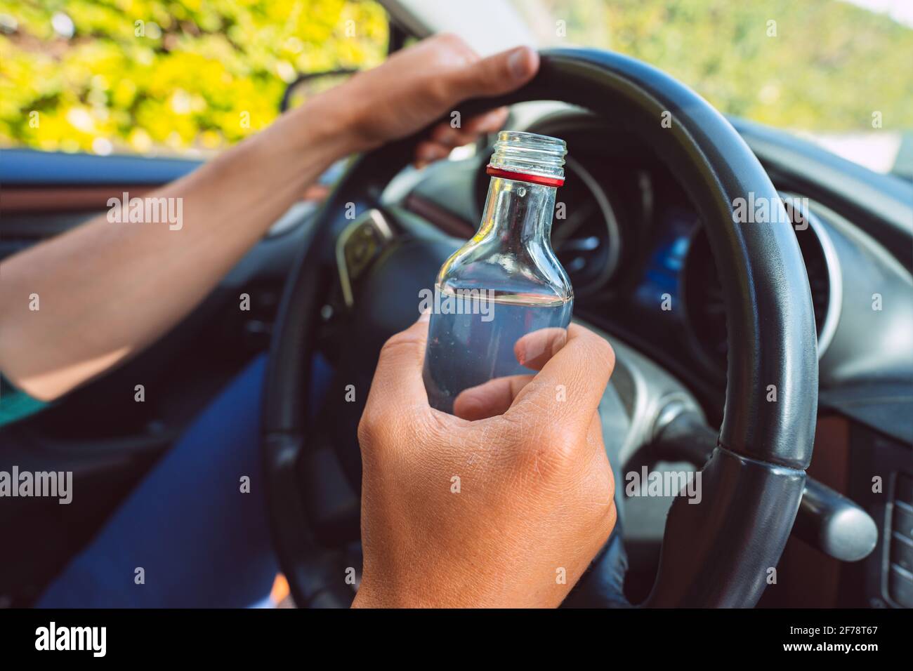 Gros plan des mains d'homme ivre sur le volant avec une bouteille de vodka. Conduite sous influence d'alcool Banque D'Images