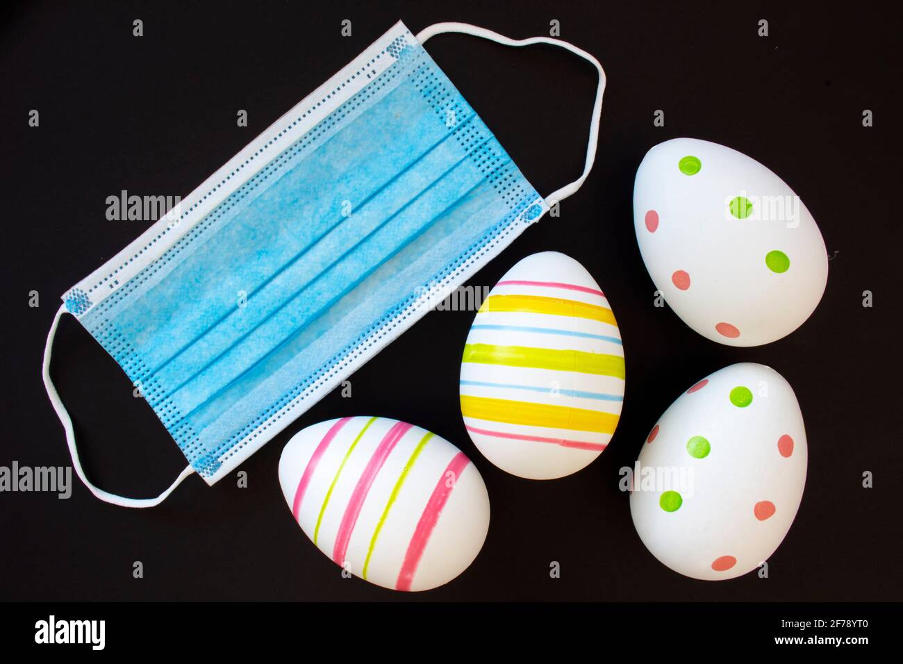 Décorez les œufs de Pâques avec un masque chirurgical sur fond noir. Concept: Pâques pendant la pandémie de Covid-19 Banque D'Images