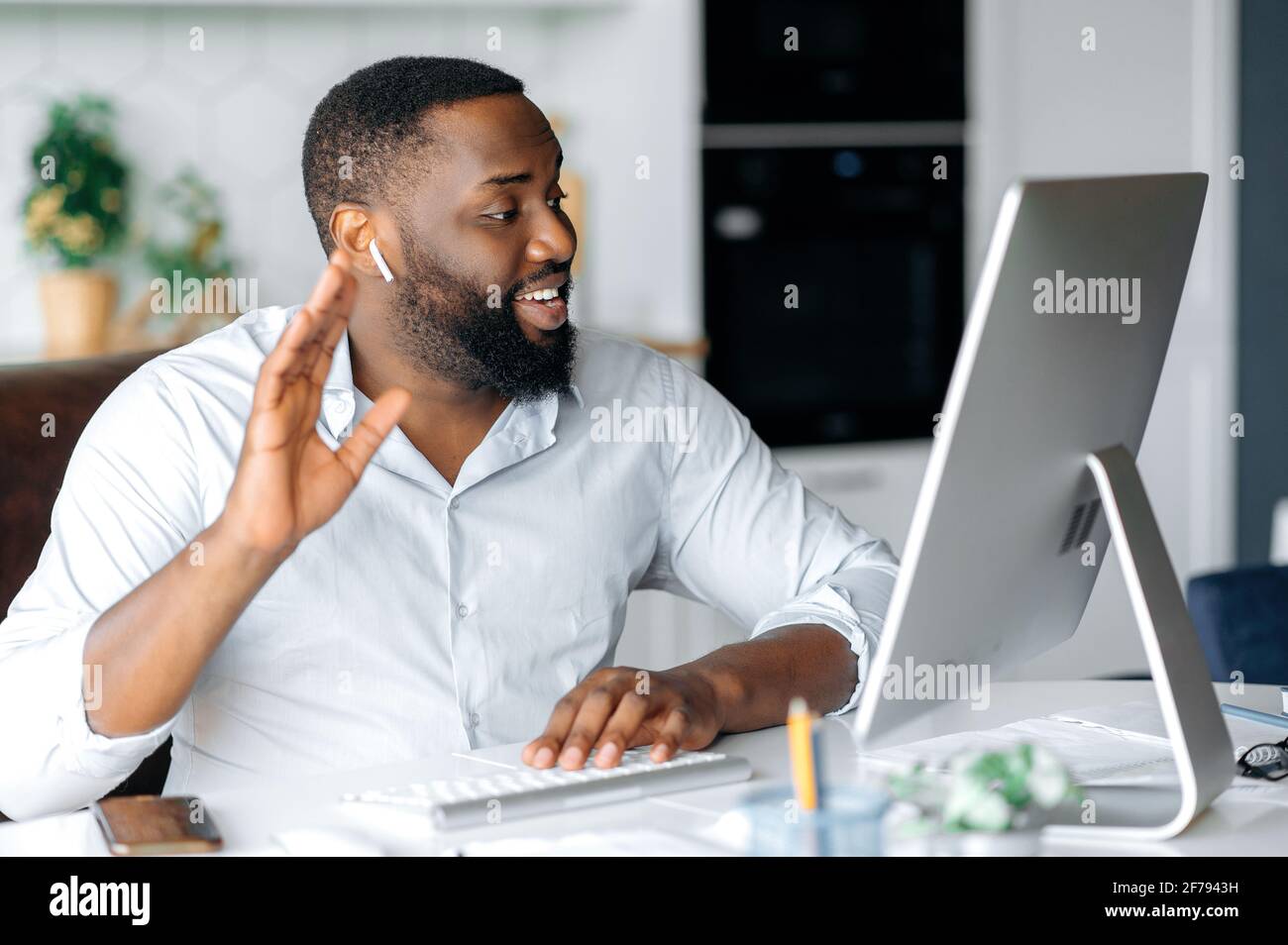 Attirant sympathique réussi jeune homme d'affaires africain américain, courtier, ou avocat travaillant à distance à l'ordinateur, parlant à un employé ou client par conférence en ligne, salutation avec le geste de la main, sourire Banque D'Images