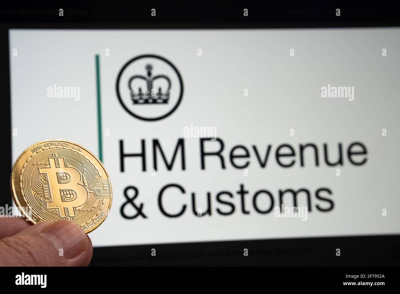 Pièce de monnaie Bitcoin tenue à la main devant le logo flou HM Revenue et Customs sur l'arrière-plan. Stafford, Royaume-Uni, 6 avril 2021. Banque D'Images