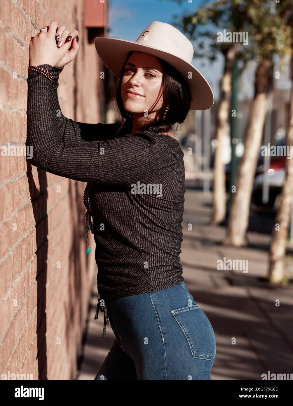 Belle femme brune posant contre un mur de briques dans une rue de ville occidentale. Boho chic cowgirl mode et style de vie concept. Banque D'Images
