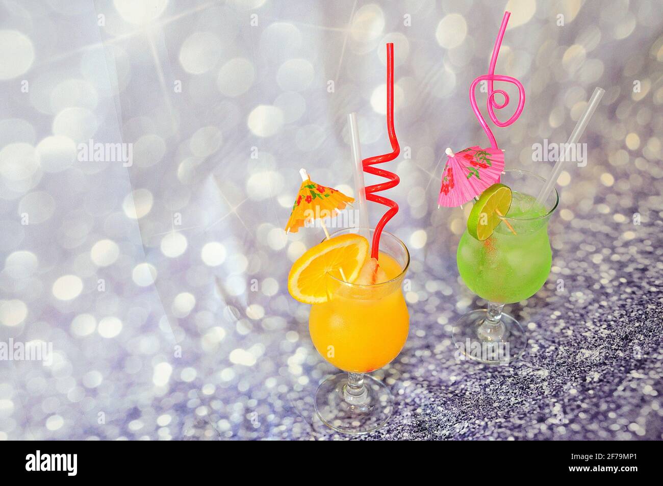 Deux verres de jus d'orange et de citron vert, décorés de parasols et de tubes à glace, ainsi que de tranches d'agrumes sur fond gris. Gros plan. Banque D'Images