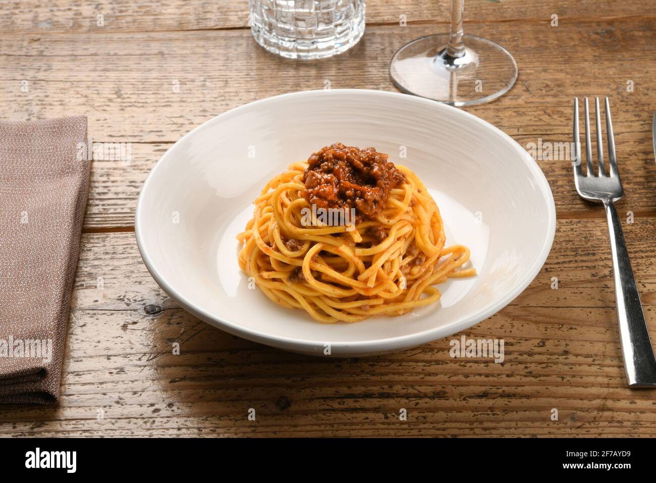 Service de ragoût de sanglier sur tagliolini ou spaghetti italien pâtes sur une table en bois avec verrerie et ustensiles un concept de spécialité régionale Banque D'Images
