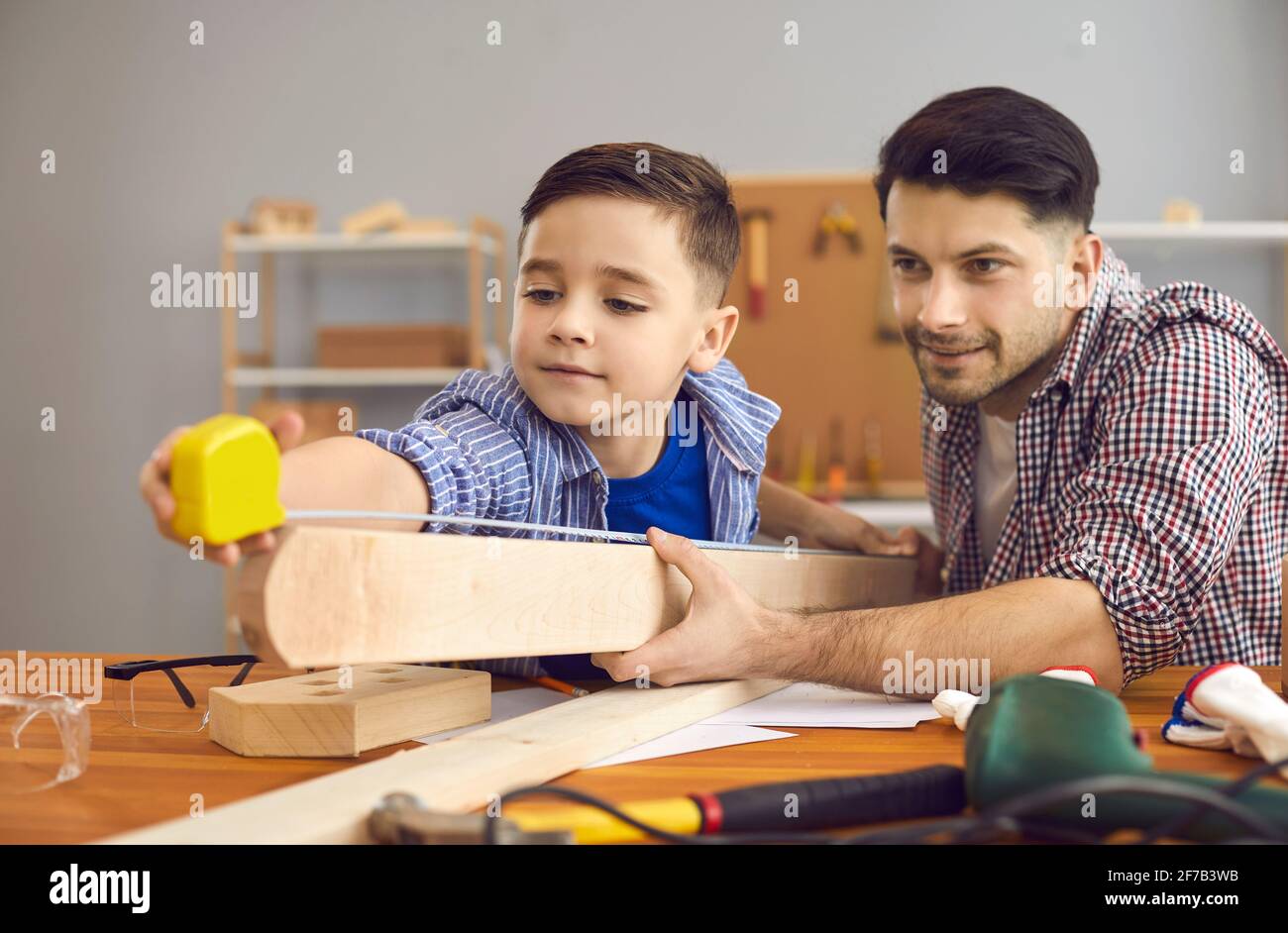 Joyeux père et fils caucasien mesurant la planche de bois avec le ruban atelier à domicile Banque D'Images