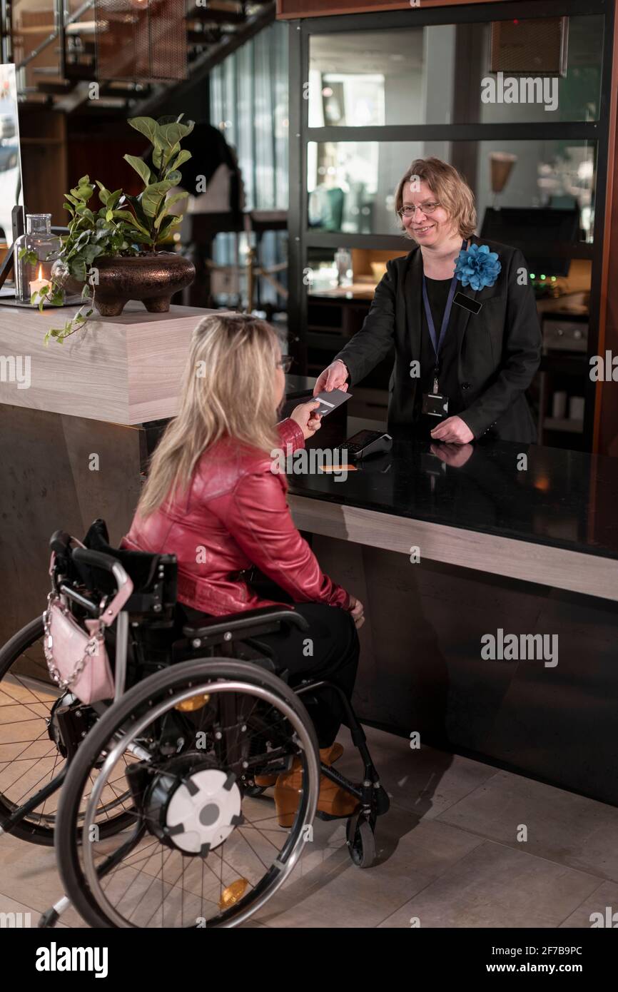 Femme en fauteuil roulant parlant à la réceptionniste Banque D'Images