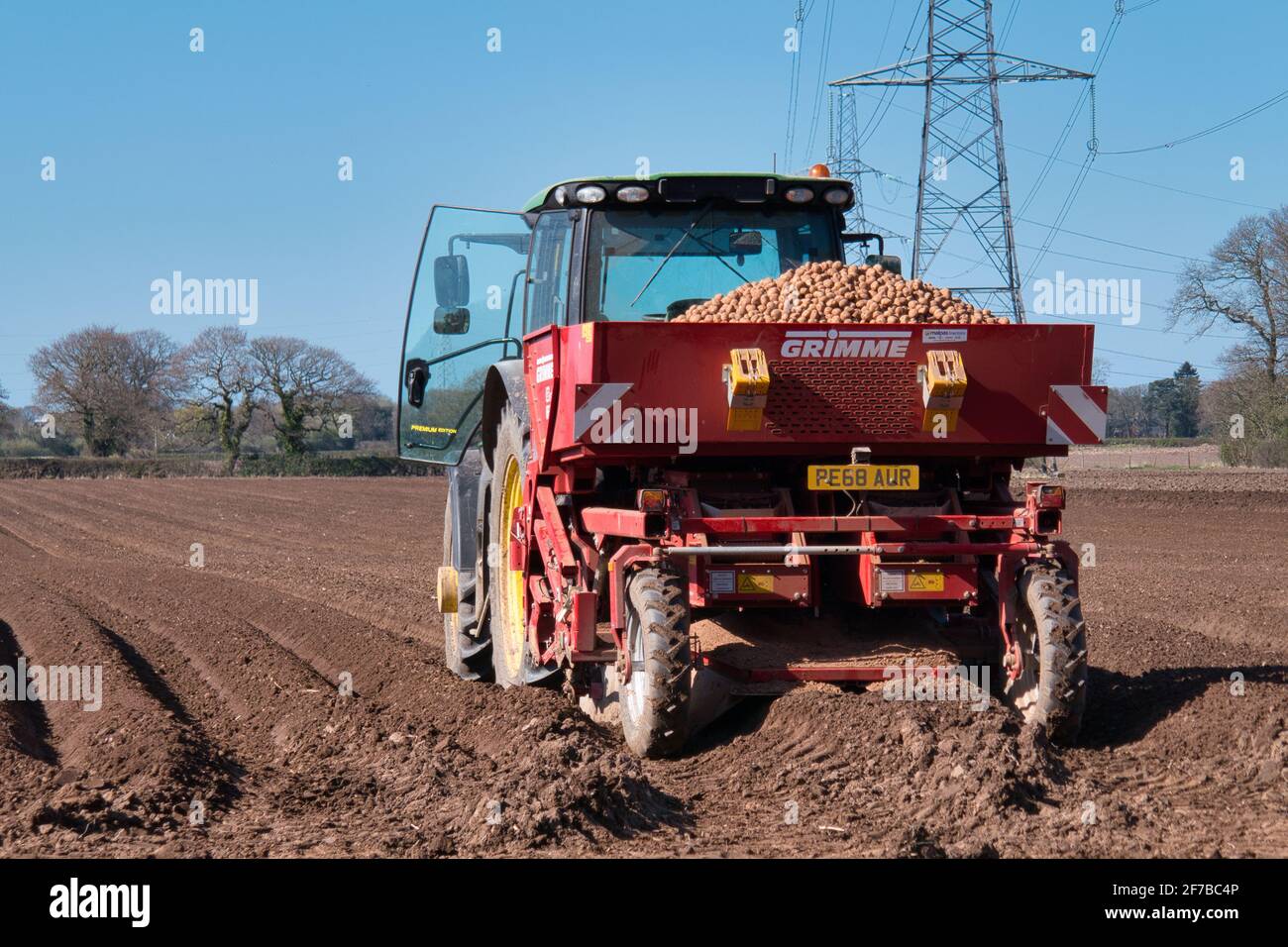 Un tracteur John Deere tractant un semoir à courroie Grimme BG215, plantant des pommes de terre sur un champ sillonné par une journée ensoleillée au printemps à Wirral, au Royaume-Uni Banque D'Images