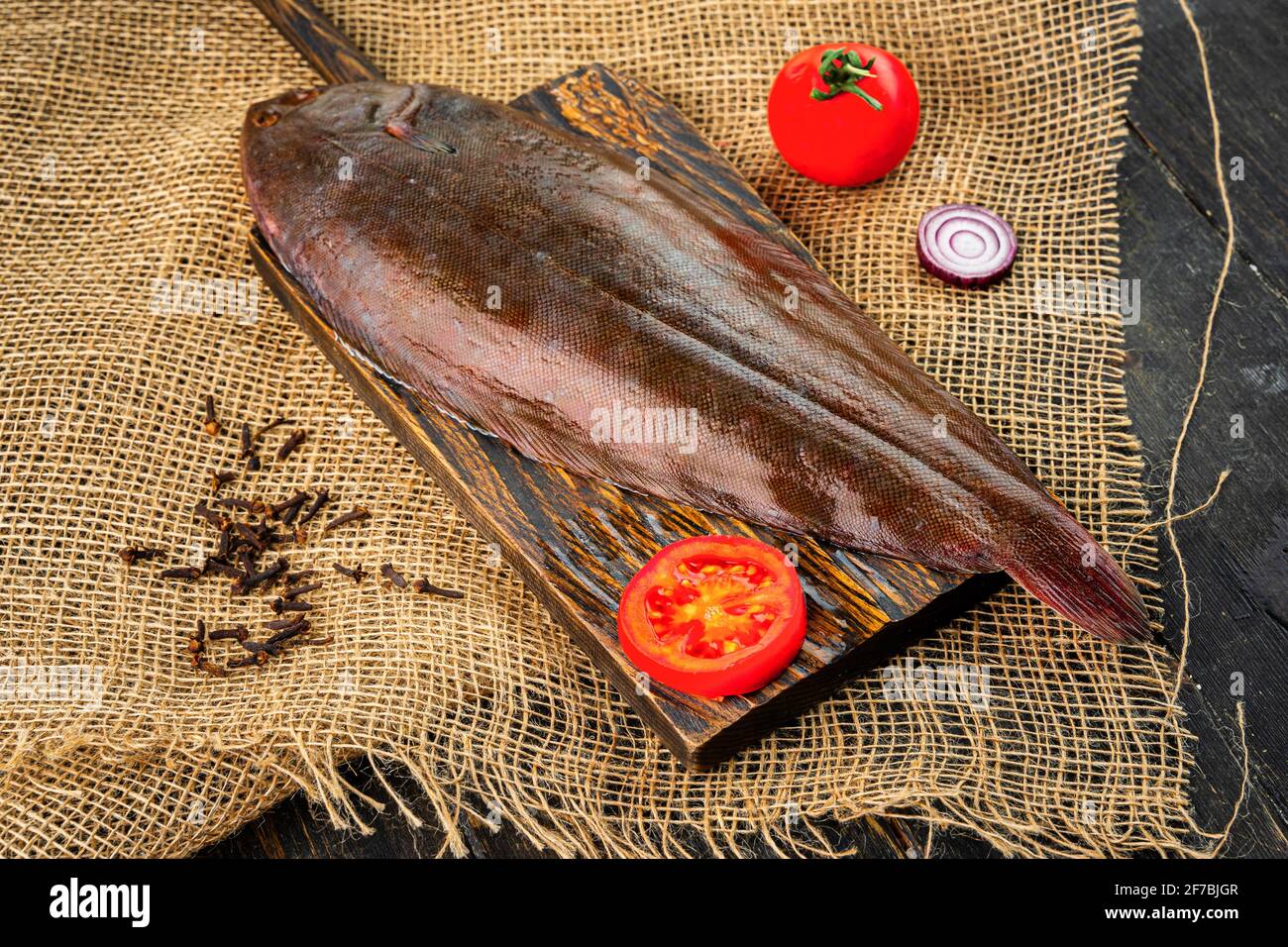 Poisson frais cru avec tomates sur une planche à découper en bois. Banque D'Images