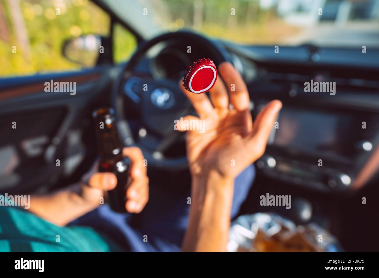Un jeune homme boit de la bière dans la voiture et jette le bouchon de la bouteille. Concentrez-vous sur le capuchon rouge en l'air. Conducteur sous influence d'alcool. Conducteur ivre Banque D'Images