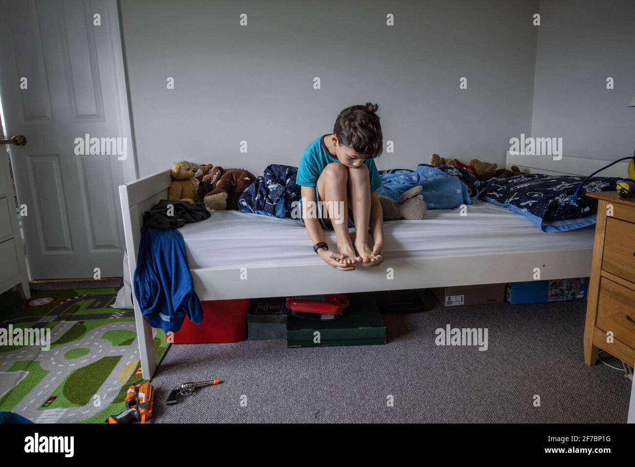 Un garçon de 7 ans s'assoit sur son lit et hésite à aller à l'école, en Angleterre, au Royaume-Uni Banque D'Images