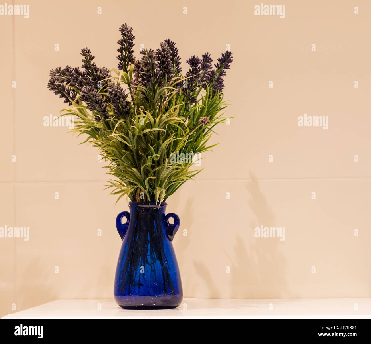 Lavande dans un vase en verre bleu sur un fond calme. Banque D'Images