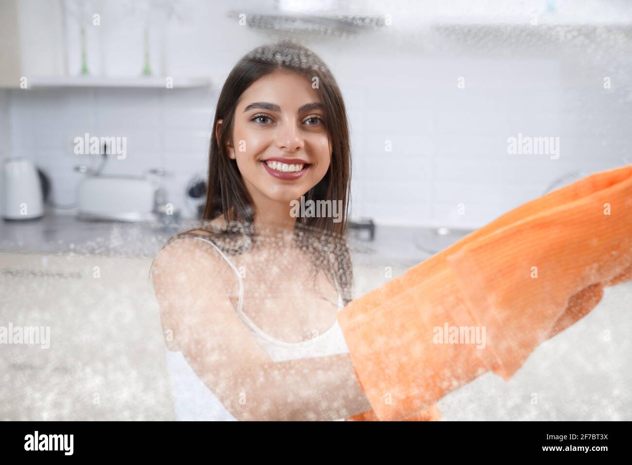 Gros plan d'une femme mignonne souriante qui lave le verre avec un chiffon dans la cuisine. Concept de nettoyage de la maison. Banque D'Images