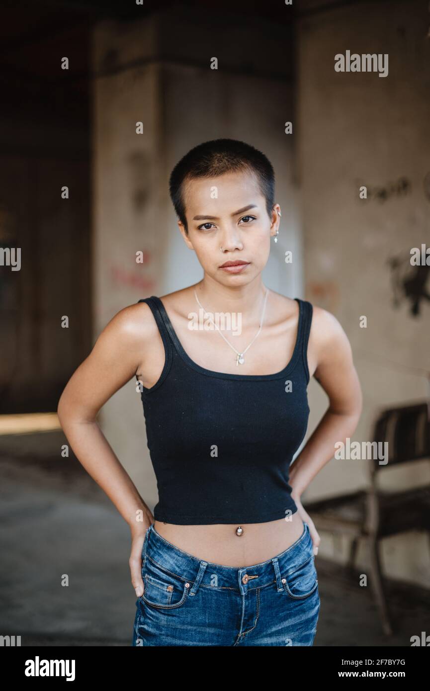 Jeune femme asiatique à cheveux courts debout dans une maison abandonnée avec ses mains à la taille regardant directement la caméra. Banque D'Images