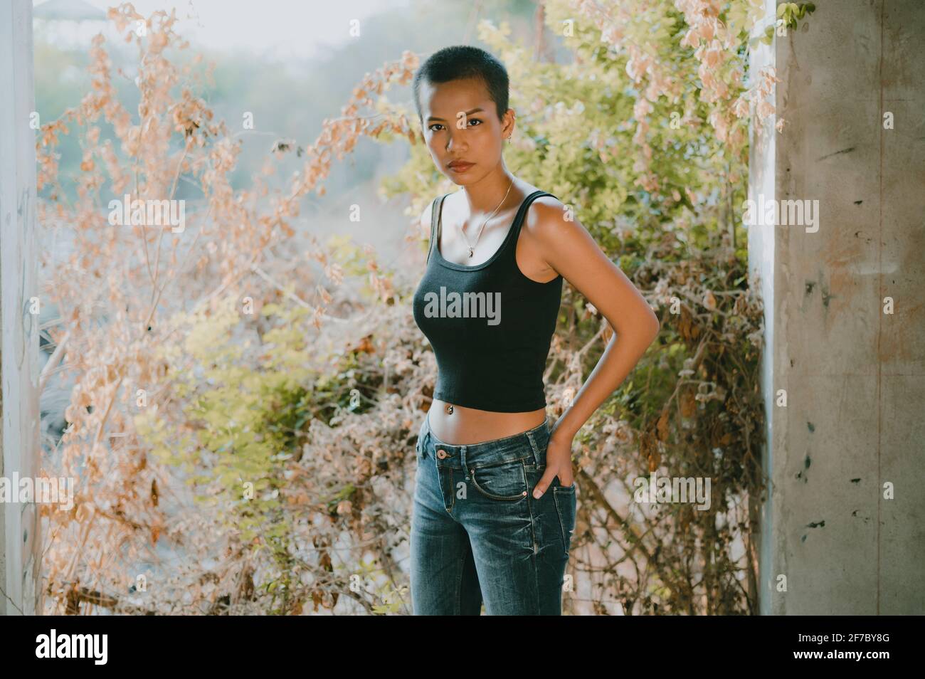 Jeune femme asiatique magnifique portant un soutien-gorge de sport debout regardant l'appareil photo, avec des fleurs floues et un fond vert Banque D'Images