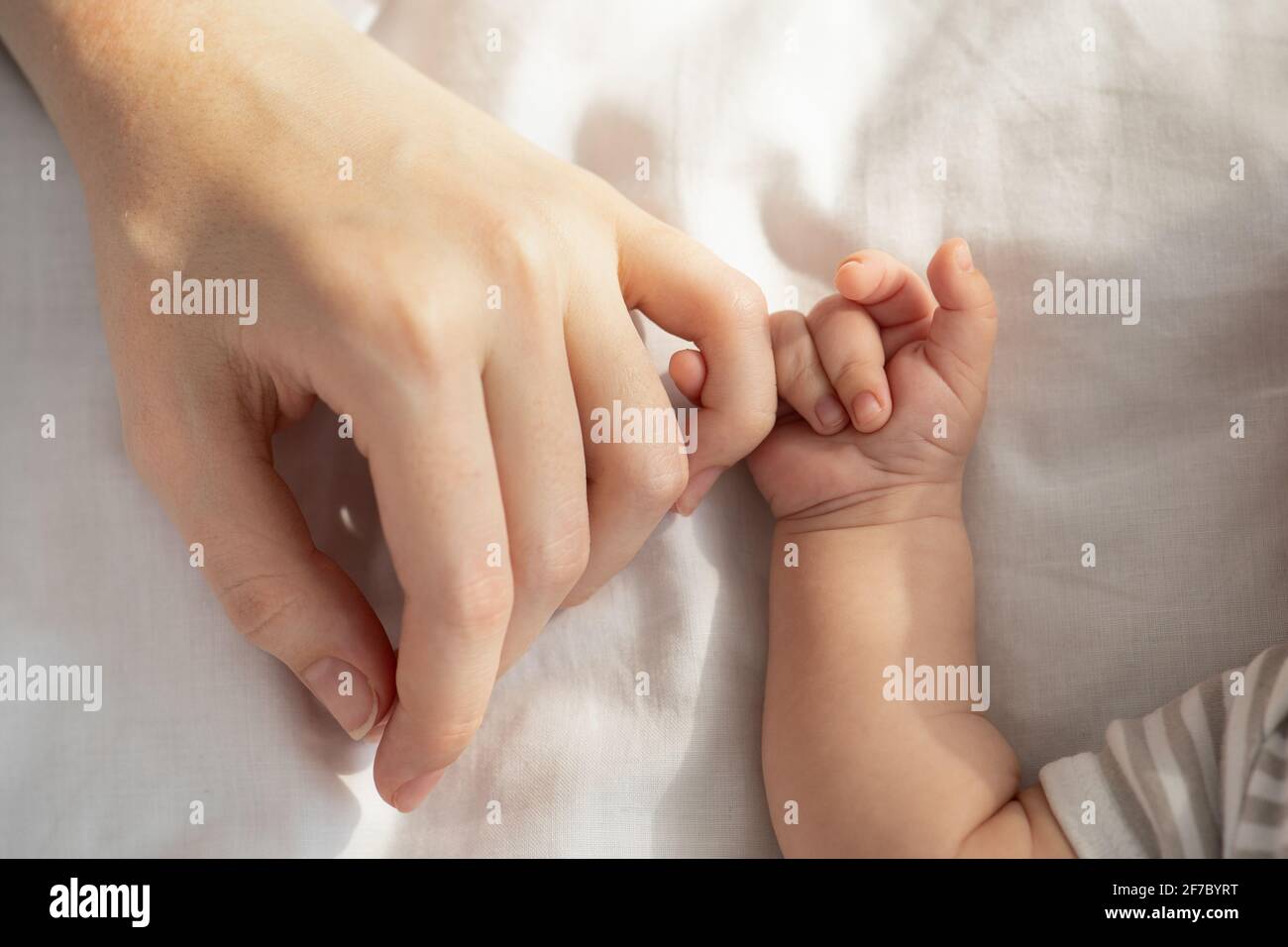 Connexion mère/bébé. Enfant nouveau-né tenant la main de la mère tout en étant allongé dans le lit Banque D'Images