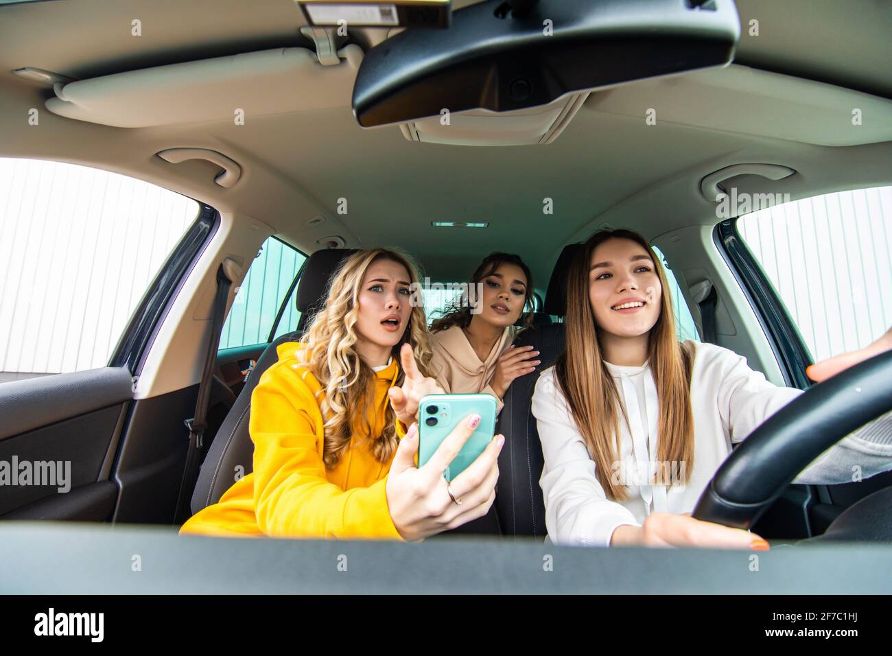 Trois amies joyeuses partent en voyage. Les femmes font le tour de la voiture, regardent le téléphone et rient. Banque D'Images