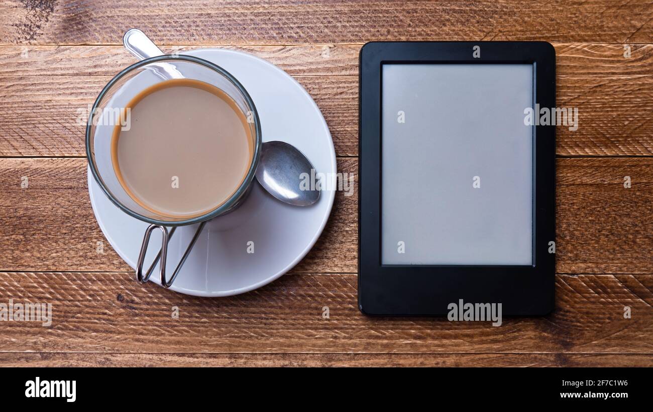 Photo d'un lecteur électronique à côté d'une tasse de café. Livre électronique, lecture électronique, lecture à la maison. Banque D'Images