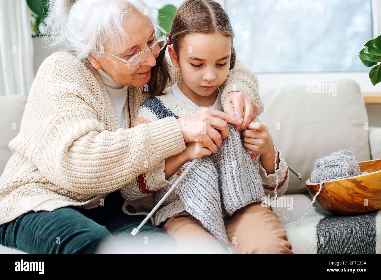 Habile granny assis sur un canapé avec sa petite-fille, elle lui apprend à tricoter, en tenant les mains au-dessus de la personne. Banque D'Images