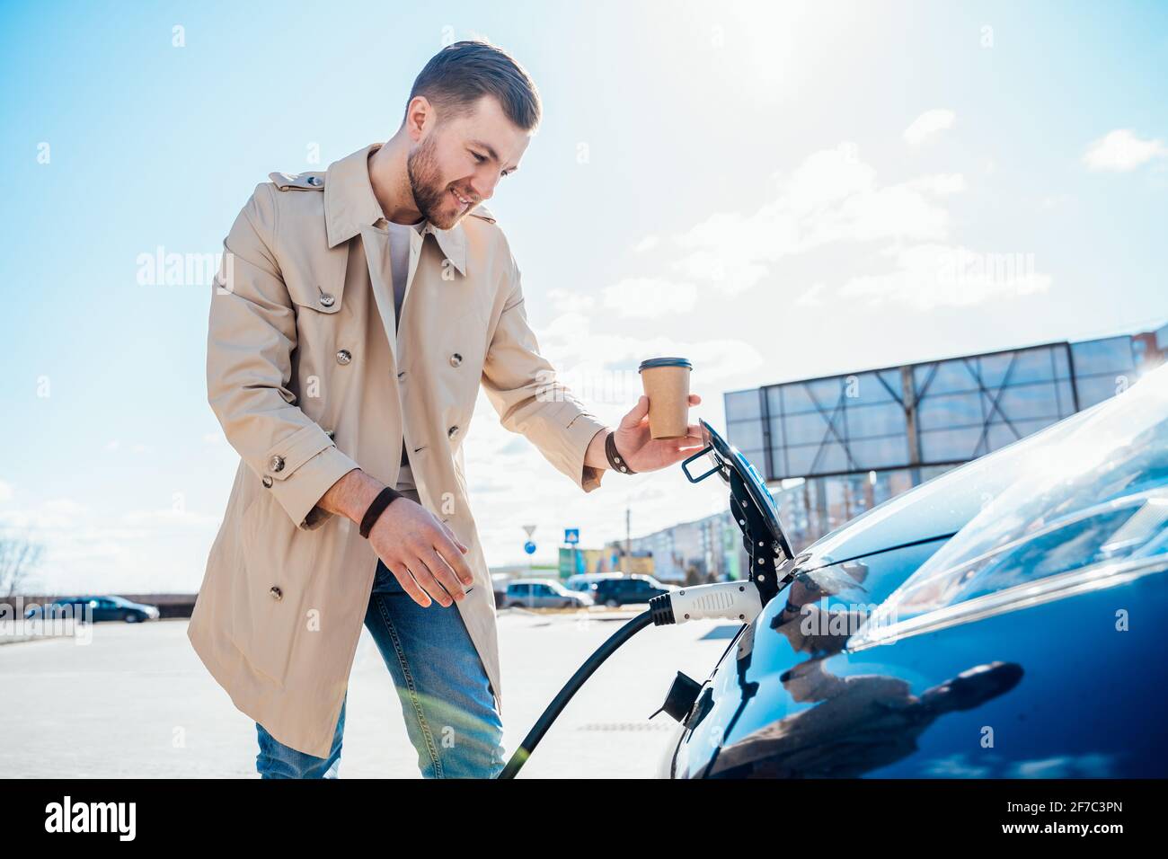 Homme élégant avec tasse à café dans les inserts à la main se branche la prise de charge de la voiture électrique Banque D'Images