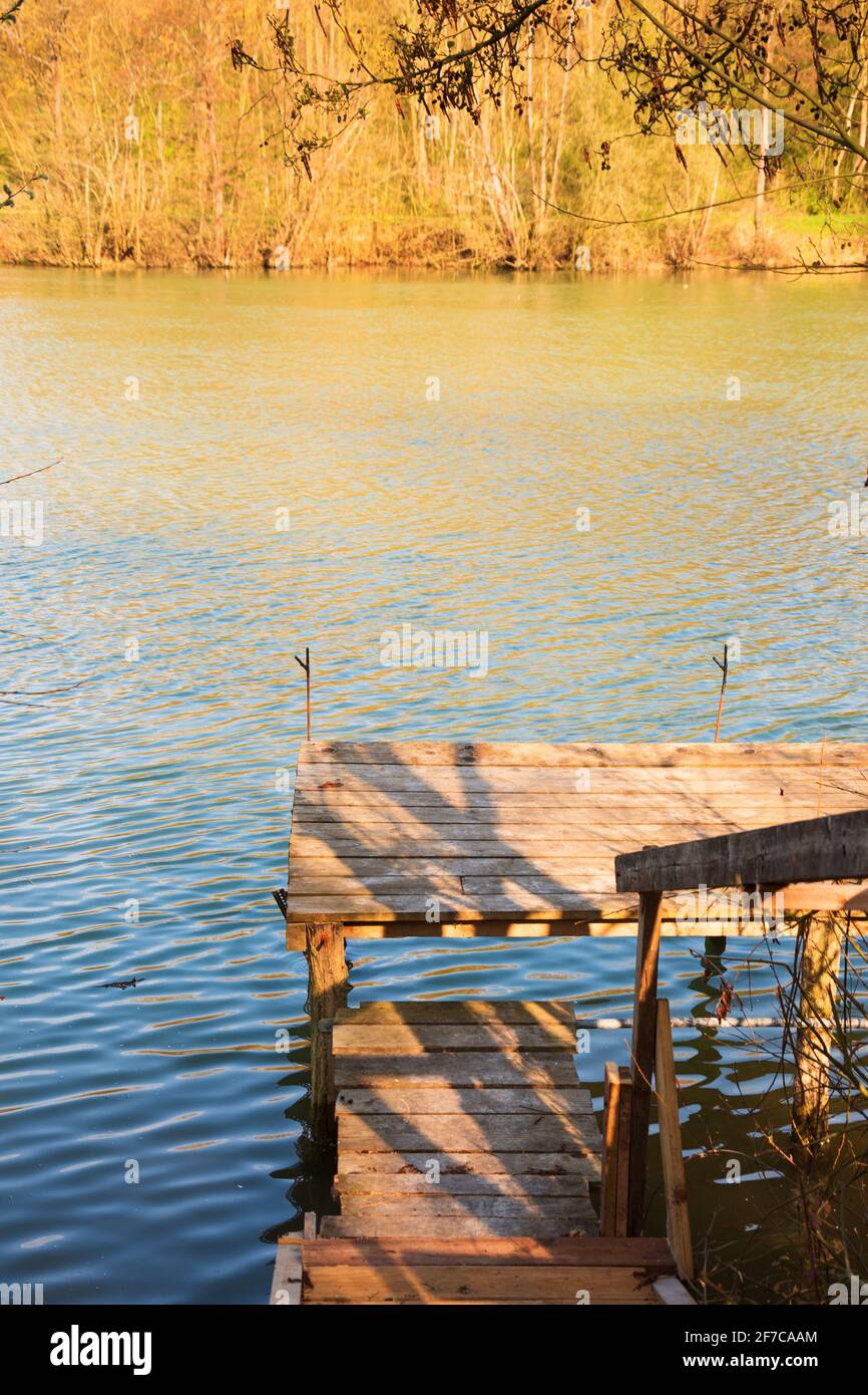 Passerelle en bois pour la pêche en rivière. Vue panoramique avec des rayons de lumière dorés au coucher du soleil réfléchis dans l'eau. Ile-de-France, France. Vacances à la campagne Banque D'Images