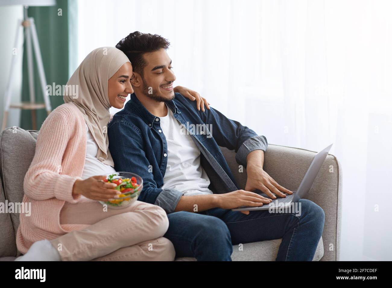 Vie domestique du couple enceinte. Les conjoints musulmans se détendent avec un ordinateur portable sur le canapé Banque D'Images