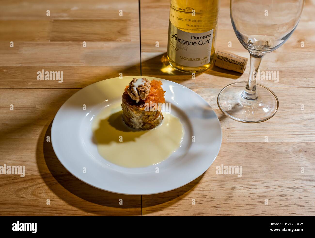Menu dégustation : dessert raffiné ou sucré servi sur une assiette blanche : gâteau aux carottes et aux noix de frangipane avec crème anglaise et vin blanc Monbazillac Banque D'Images