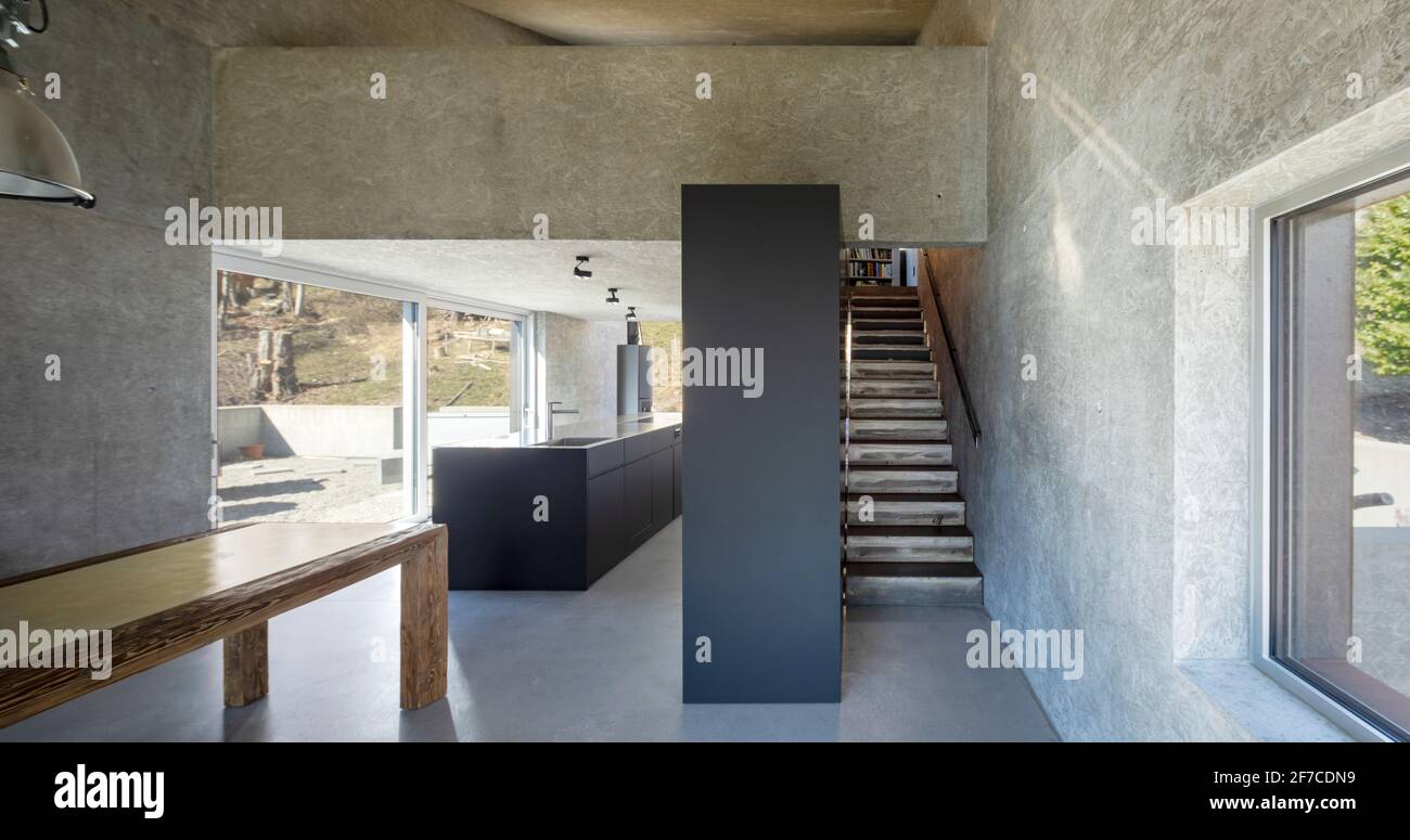 Vue sur l'avant de l'espace ouvert dans une villa moderne avec cuisine, escalier minimal et table. Grandes fenêtres. Personne à l'intérieur Banque D'Images