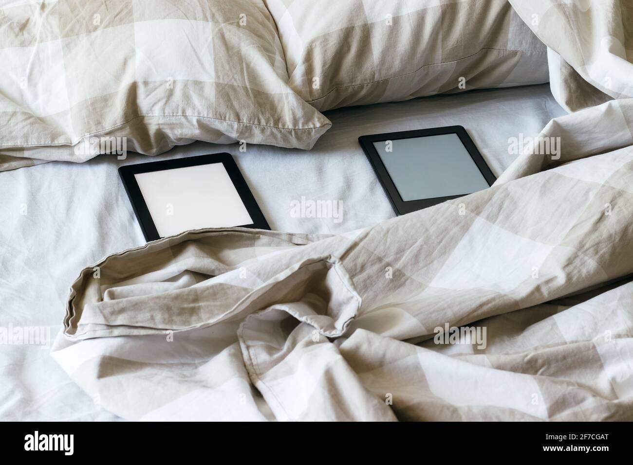 Deux livres électroniques modernes avec un écran vide vierge sur un lit blanc et beige. Tablettes de la famille Mockup sur la literie Banque D'Images