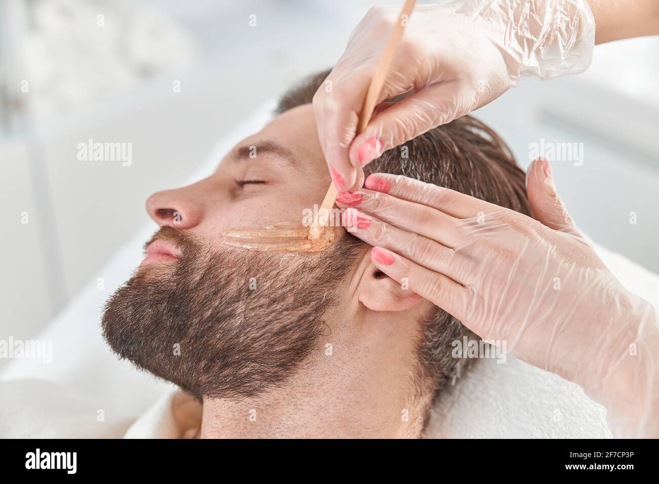 Concept de la cosmétologie et du visage. Une esthéticienne réalise des  modèles de visage et de barbe pour une épilation à la cire par un homme.  Épilation à la cire Photo Stock -
