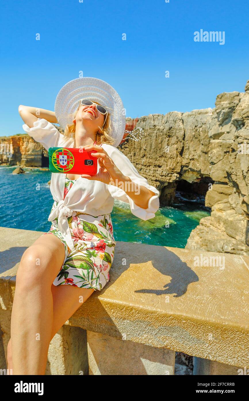 Femme prend selfie à Boca do Inferno à Cascais, Océan Atlantique, Portugal.Tourisme féminin prend des photos par téléphone portable avec le drapeau portugais de l'Enfer Banque D'Images