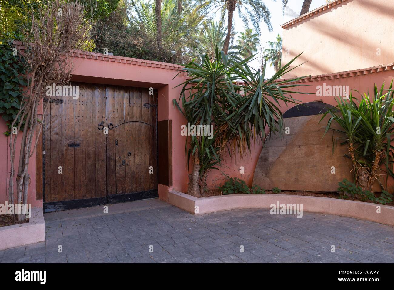 Porte en bois dans un mur peint rougeâtre avec une large porte à l'avant et un immense jardin derrière dans la belle ville de Marrakech, au Maroc Banque D'Images