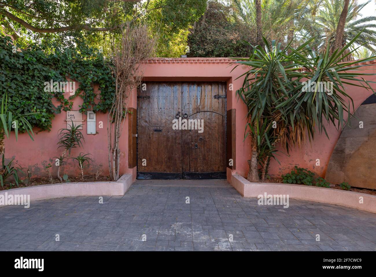 Porte en bois dans un mur peint rougeâtre avec une large porte à l'avant et un immense jardin derrière dans la belle ville de Marrakech, au Maroc Banque D'Images