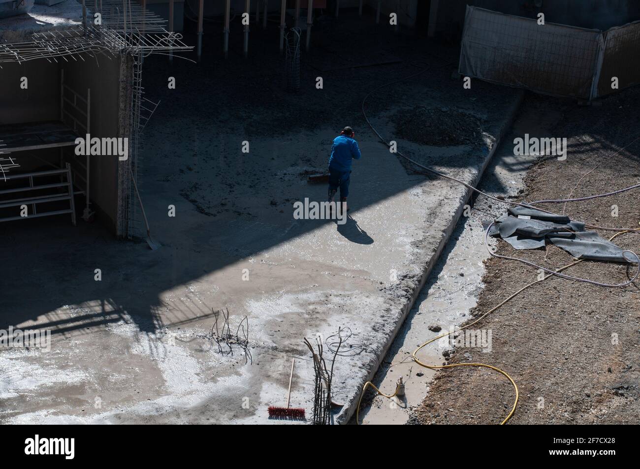 un chantier de construction avec un homme méconnaissable avec des protections auditives nettoyage du sol en béton à l'aide d'un balai Banque D'Images