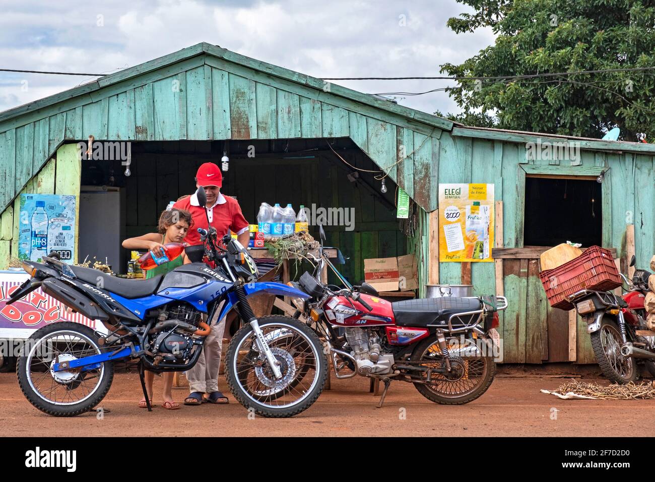 Boutique primitive / station-service avec moto de remplissage enfant avec gasolène de bouteille en plastique à la ville Edeira dans la campagne Itapua, Paraguay Banque D'Images