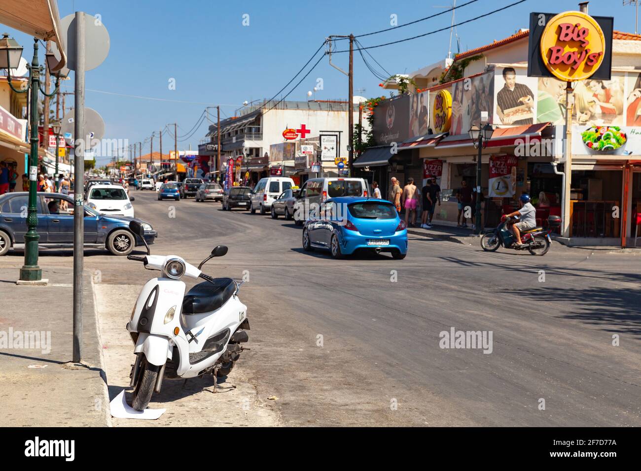 Zakynthos, Grèce - 14 août 2016 : le scooter blanc est stationné dans la rue de la station balnéaire de Laganas. Les gens ordinaires marchent dans la rue Banque D'Images