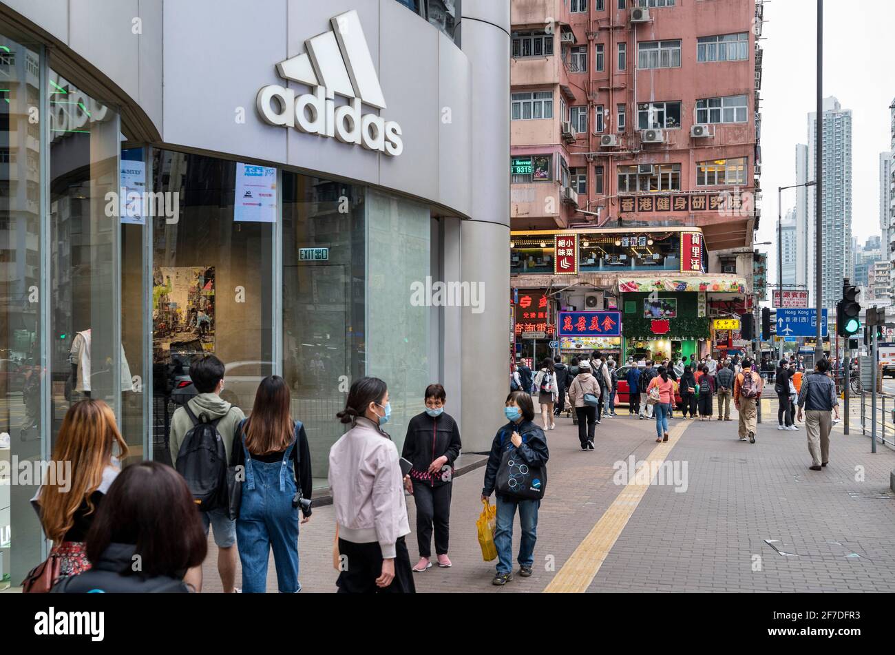 Des piétons marchent devant la marque allemande multinationale de vêtements de sport Adidas magasin et logo à Hong Kong. Banque D'Images