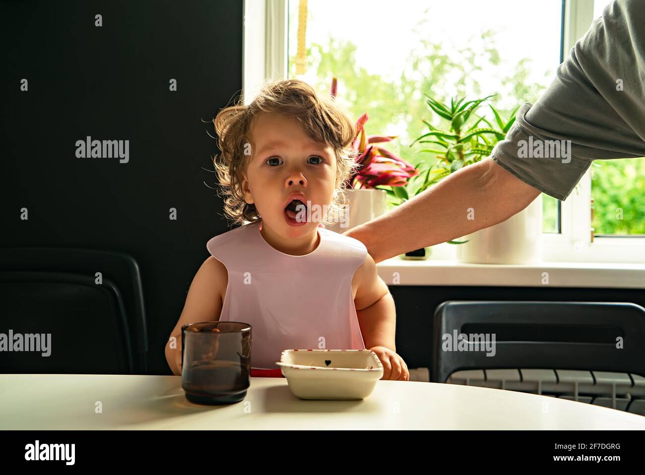 Portrait d'un petit enfant étouffé sur la nourriture manger à l'intérieur la cuisine et un parent claque sa main sur le retour Banque D'Images