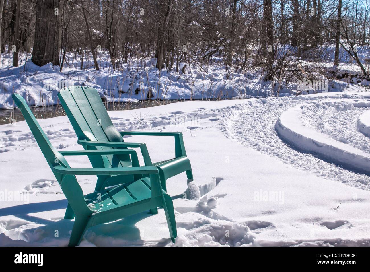 Chaises turquoise Adirondack dans une banque de neige dans le sud-ouest, Ontario, Canada le long d'un ruisseau glacé, 2021. Banque D'Images
