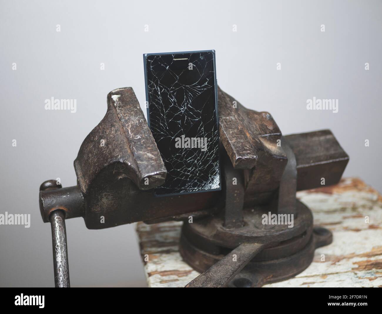 Le téléphone dont l'écran est fissuré est fixé dans un ancien etau Banque D'Images