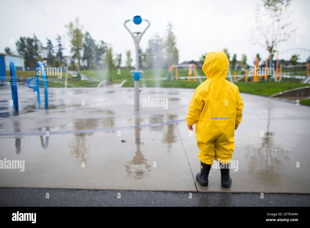 Tout-petit en costume de pluie et bottes regarde l'eau garez-vous par temps humide Banque D'Images